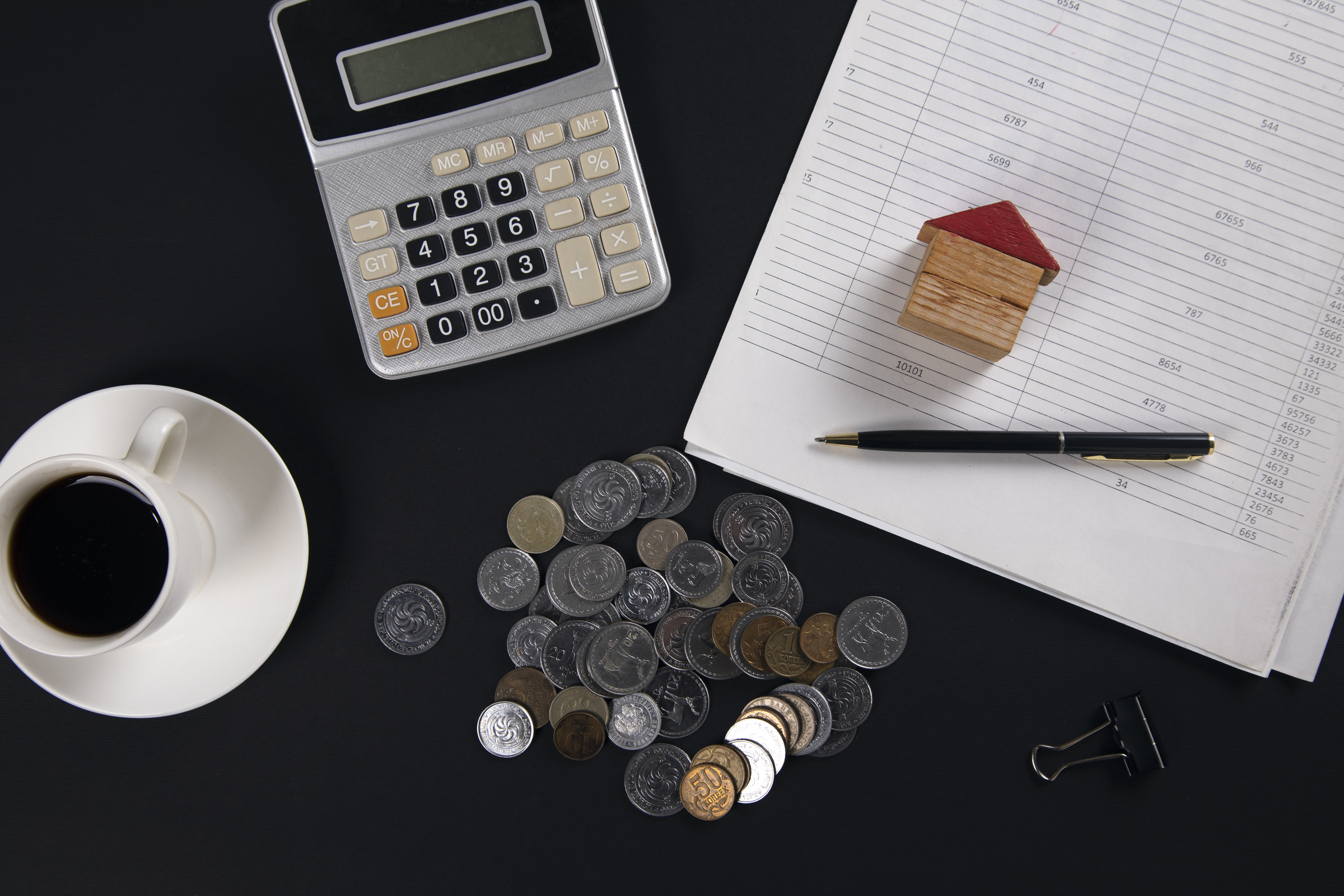 coins with house model on document with  calculator and coffee on table